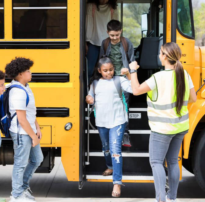 School Bus driver gives students fist bump - 1 Female school bus driver wearing reflective best gives students fist bump as they get off the bus